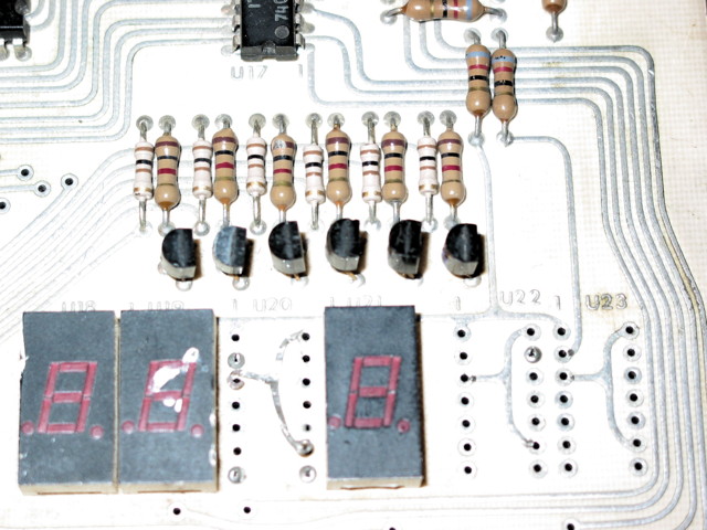 A closeup of a KIM-1's display area with 6 transistors nicely lined up.  The seven-segment displays are beat up quite a bit and there are some traces lifted off the circuit board.
