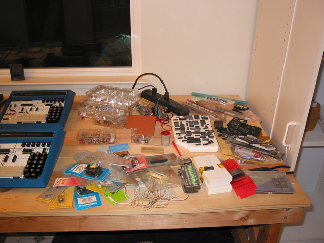 Wooden bench with two Heathkit ET-3400 microprocessor trainers and electronic parts strewn all over the remaining space.