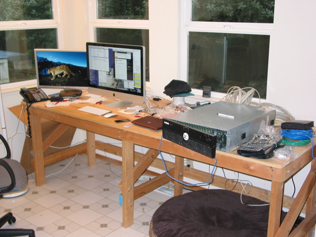 A wooden workbench with an iMac and tons of computer junk on it