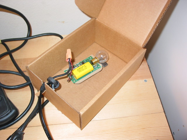 A circuit board with an ultraviolet lightbulb sitting inside a cardboard box with a lid.